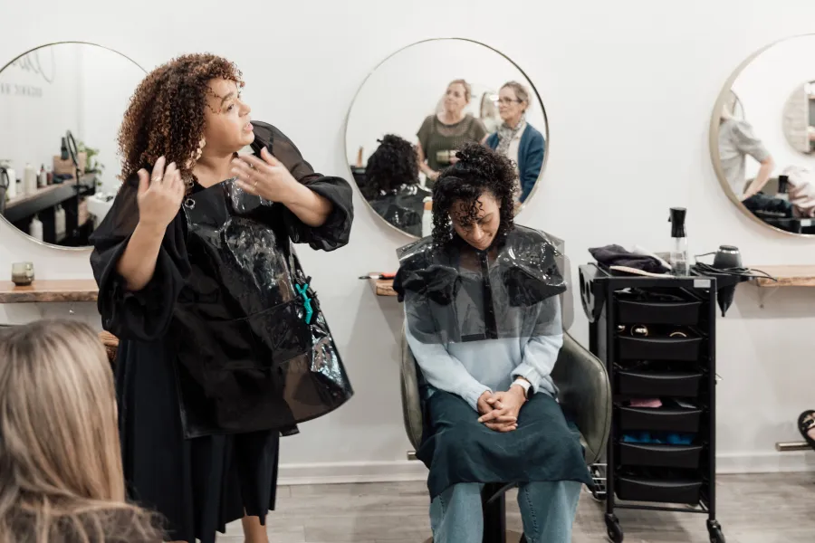 Caroline Smalley explaining a technique to stylists at a Curl Identity education day, with a model gowned and seated ready for the demonstration